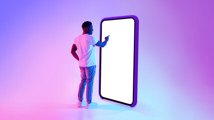 Poster - Black guy standing near big cellphone with mockup for your app on screen, interacting with user interface in neon light