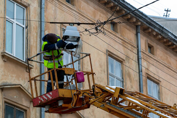 The electrician replaces the light bulb in the street lamp, being in the basket of the lift.	