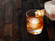 Liquor being poured over an artisan ice ball on a rustic wooden background.