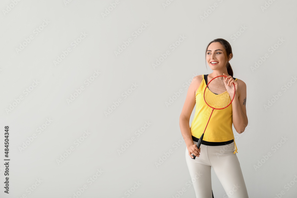 Sporty female badminton player on light background