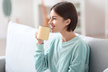 Wall Mural - Beautiful young woman drinking tasty tea on sofa at home