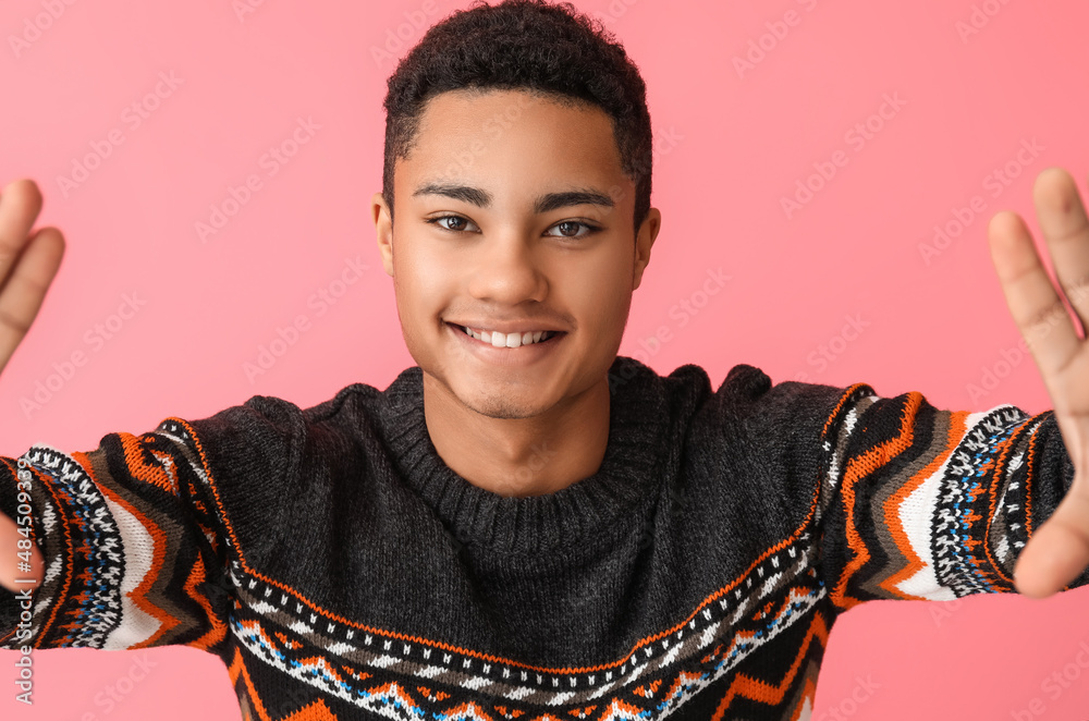 Handsome African-American guy in knitted sweater on color background