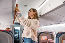 Young Woman Putting Travel Bag In Cabin Compartment