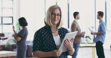 Poster - She stands out in the office. Young businesswoman browsing on a digital tablet device in a busy office with her coworkers in the background. Confident caucasian woman smiling while planning online