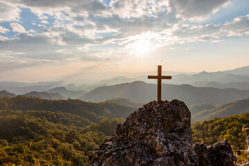 Wall Mural - Crucifix symbol on top rock  mountain with bright sunbeam on the colorful sky background. Silhouettes