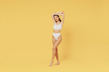 Full size young sexy brunette woman 20s wear white underwear with perfect fit body raise up hands close eyes isolated on plain yellow color background studio portrait. People female beauty concept