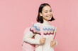 Smiling happy teen student girl of Asian ethnicity wear sweater backpack hold books listen music in earphones isolated on pastel plain light pink background Education in university college concept