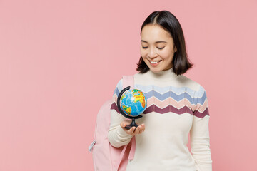 Wall Mural - Smiling teen student girl of Asian ethnicity wear sweater backpack hold books hold in hands Earth world globe isolated on pastel plain light pink background Education in university college concept