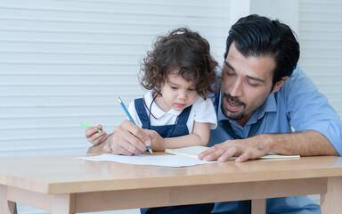 Caucasian young father with beard teaching little cute daughter writing or drawing on book in living room after work. Happy handsome dad help kid learning at home