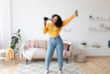 Positive Young African American Woman Using Hair Dryer As Microphone, Singing And Dancing, Having Fun At Home