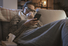 Sick woman resting on the couch and connecting with her smartphone