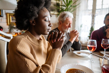 Happy multiethnic family praying before meal at home together. People religion concept