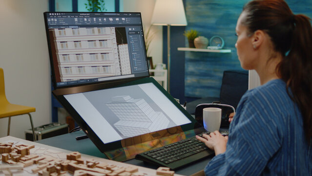 Businesswoman working on building model with touch screen in architectural office. Architect using computer for construction layout and blueprint plan with maquette on table. Graphic engineer