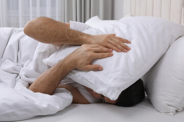 Canvas Print - Handsome man sleeping under pillow in bed at home