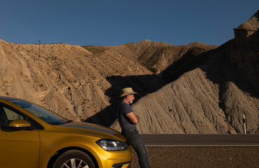 Adult man in cowboy hat standing against car on desert against mountain. Almeria, Spain