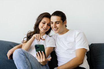 Happy young couple sitting on a couch at home looking at mobile phone