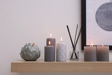 Burning Candles And Air Freshener On Wooden Shelf Indoors