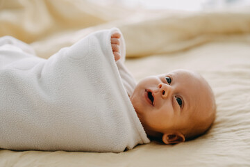 newborn baby wrapped in a blanket lying in bed, smiling.