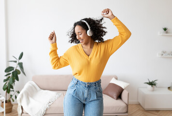 Canvas Print - Happy young black woman in headphones dancing with closed eyes at home