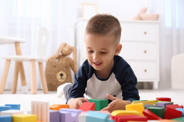 Poster - Cute little boy playing with colorful building blocks on floor in room