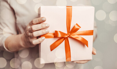 Woman hands holding surprise gift box present wrapped paper with red bow on pastel pink background. 8 march, birthday, mother's day