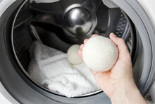 Woman Using Wool Dryer Balls For More Soft Clothes While Tumble Drying In Washing Machine Concept. Discharge Static Electricity And Shorten Drying Time, Save Energy.