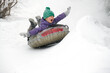 Cute child boy riding on snow tubing rising hands up. Kid sledding slide down hill. Winter fun activity outdoor.