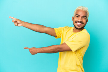 Wall Mural - Young Colombian handsome man isolated on blue background pointing finger to the side and presenting a product