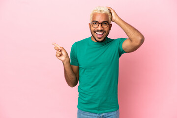 Wall Mural - Young Colombian handsome man isolated on pink background surprised and pointing finger to the side