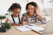 African-american mom mother tutor nanny childminder helping assisting with homework school project to a preteen daughter. Homeschool concept. E-learning on laptop