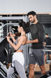 © LIGHTFIELD STUDIOS - Arabian trainer standing near middle east sportswoman and leg press machine in gym.