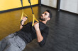 © LIGHTFIELD STUDIOS - Bearded muslim sportsman training with suspension straps in gym.