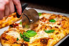 Chef Hand With Cutter Cutting Pizza To Pieces At Pizzeria