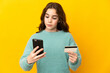 © luismolinero - Little caucasian girl isolated on yellow background buying with the mobile with a credit card