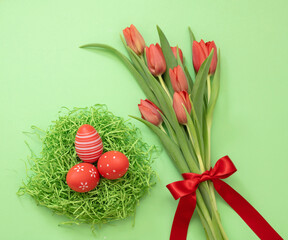 Easter Spring Holiday celebration. Egg nest and fresh red tulip on green background, overhead