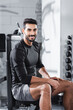 © LIGHTFIELD STUDIOS - Smiling arabian sportsman looking at camera while sitting on sports equipment in gym.