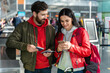 © NFstock - Happy husband and wife standing together at the airport and checking tickets details at the smartphone. Stock photo