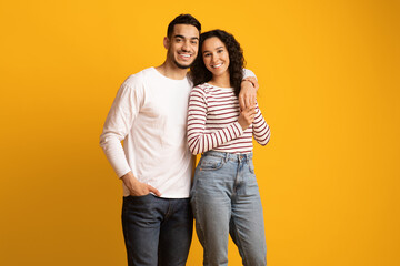 Wall Mural - Portrait of happy embracing middle eastern couple posing over yellow background