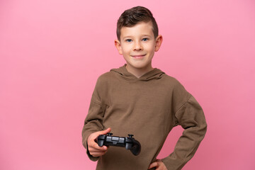 Wall Mural - Little caucasian boy playing with a video game controller isolated on pink background posing with arms at hip and smiling