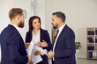 © Studio Romantic - Business people discuss contract to work together during meeting in modern office. Two men and woman in business suits stand with documents in hand and talk. Teamwork and partnership concept.