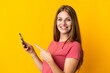 © luismolinero - Young woman using mobile phone isolated on yellow background and pointing it