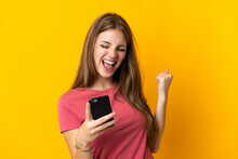Young Woman Using Mobile Phone Isolated On Yellow Background Celebrating A Victory