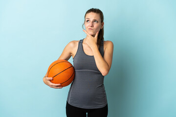 Wall Mural - Young woman playing basketball isolated on blue background having doubts