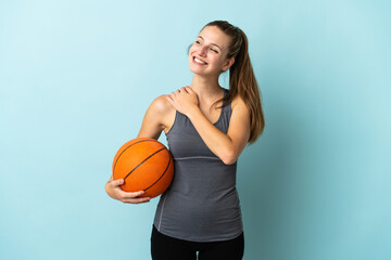 Wall Mural - Young woman playing basketball isolated on blue background looking up while smiling