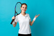 © luismolinero - Young woman tennis player isolated on blue background extending hands to the side for inviting to come