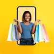 Excited black woman coming out screen with shopping bags