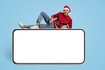 Leinwandbilder - Mobile Ad. Happy Guy Wearing Santa Hat Lying Above Big Blank Smartphone