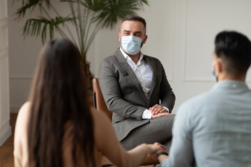 Wall Mural - Young couple sitting at therapy session with therapist in facemask