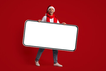 Poster - Young Cheerful Man In Santa Hat Holding Big Blank Smartphone In Hands