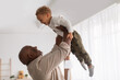 African Grandpa Holding Little Grandson Up In Air At Home